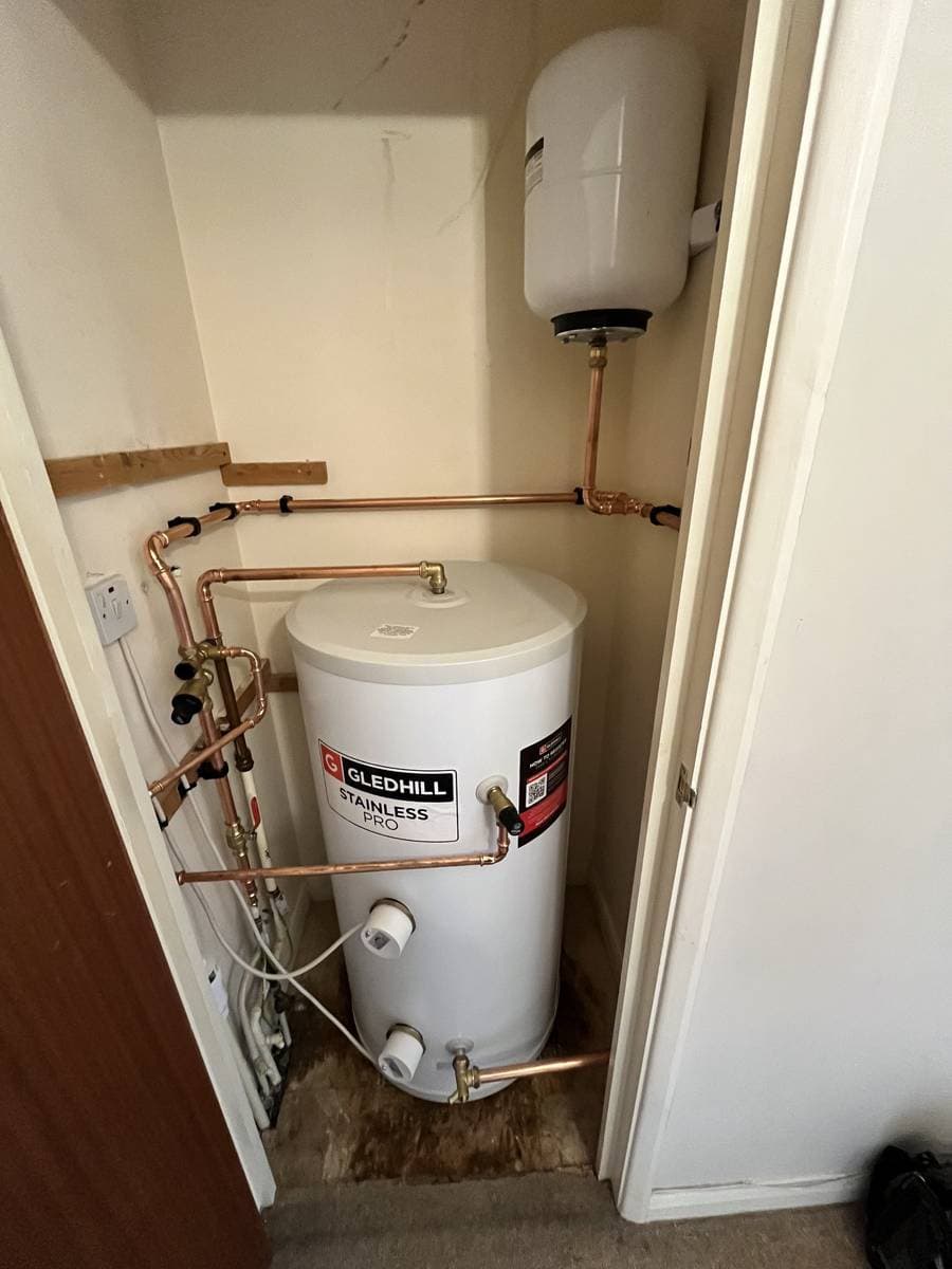 Hot water cylinder and exposed copper pipework inside a narrow cupboard